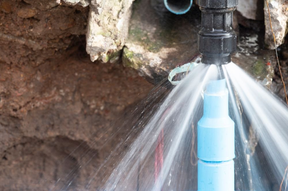 Water spraying from a burst pipe fitting inside an open wall